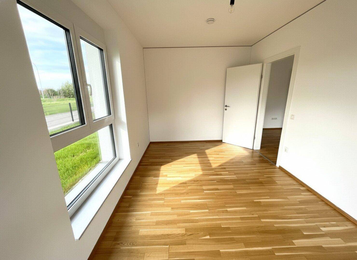 Helles Schlafzimmer mit Parkettboden und großen Fenstern, ideal für individuelle Einrichtung.