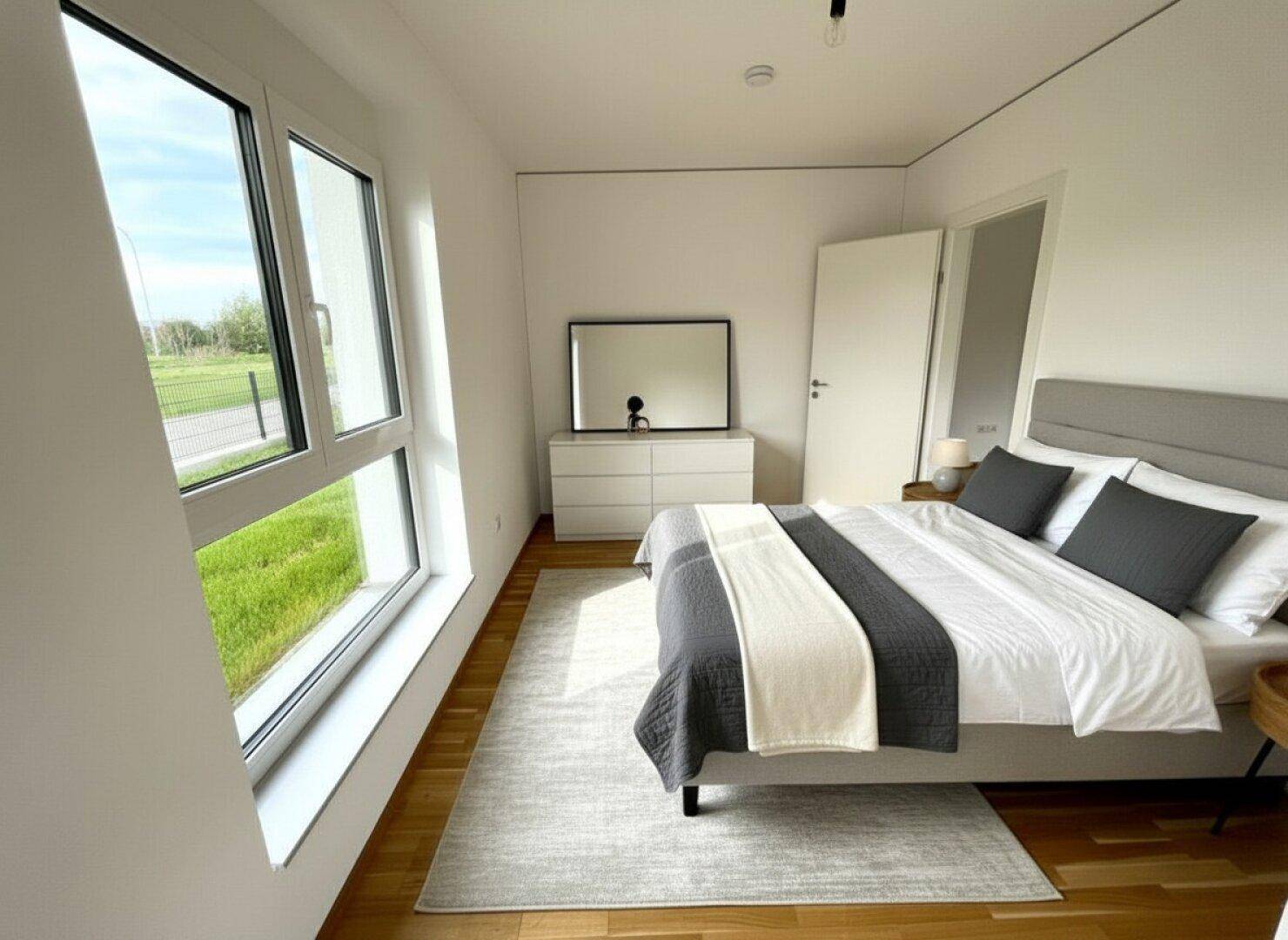 Modernes Schlafzimmer mit großen Fenstern, Parkettboden und Blick ins Grüne.