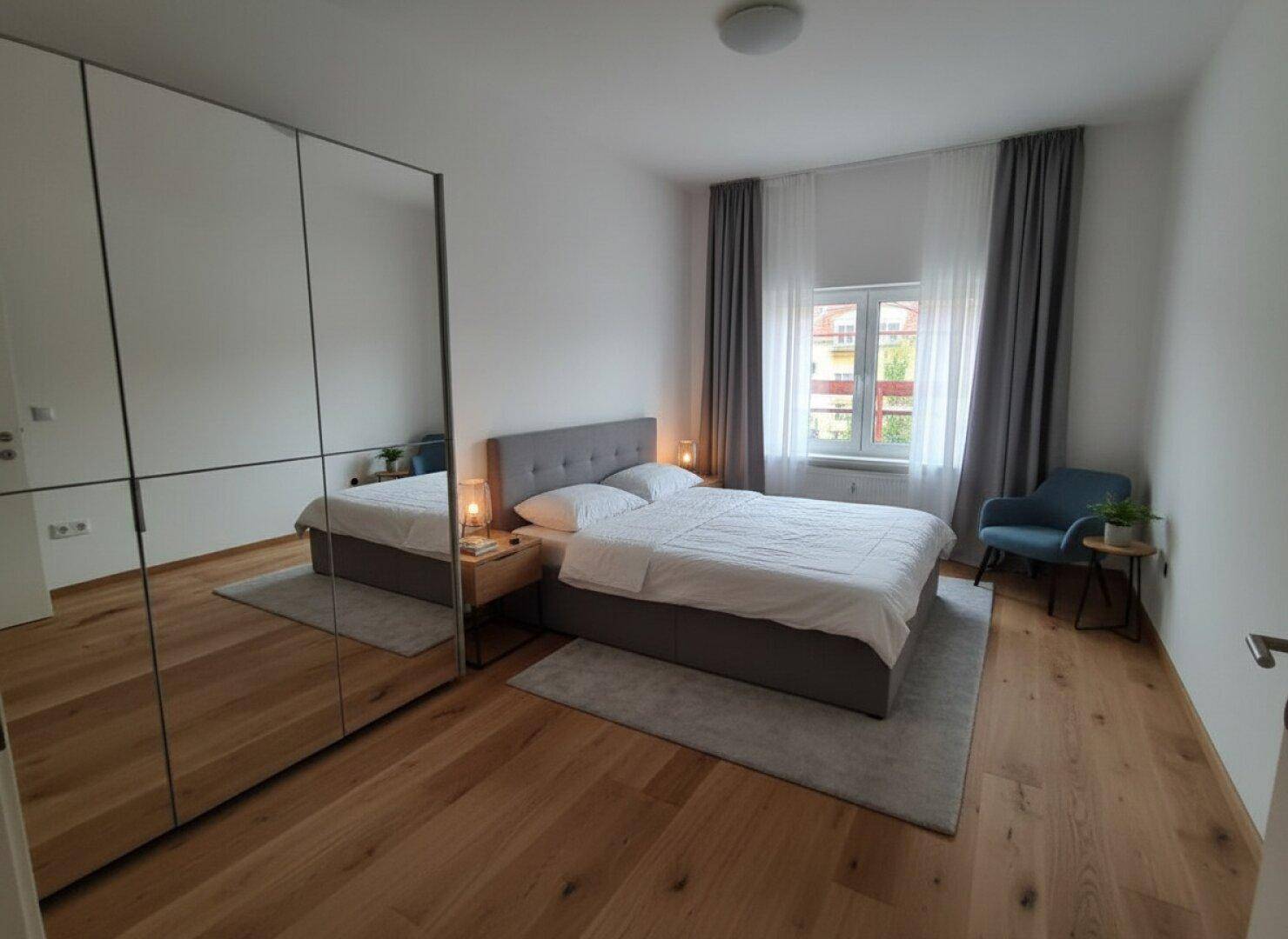 Helles Schlafzimmer mit Holzboden, großem Bett und Spiegelschränken, modern eingerichtet.
