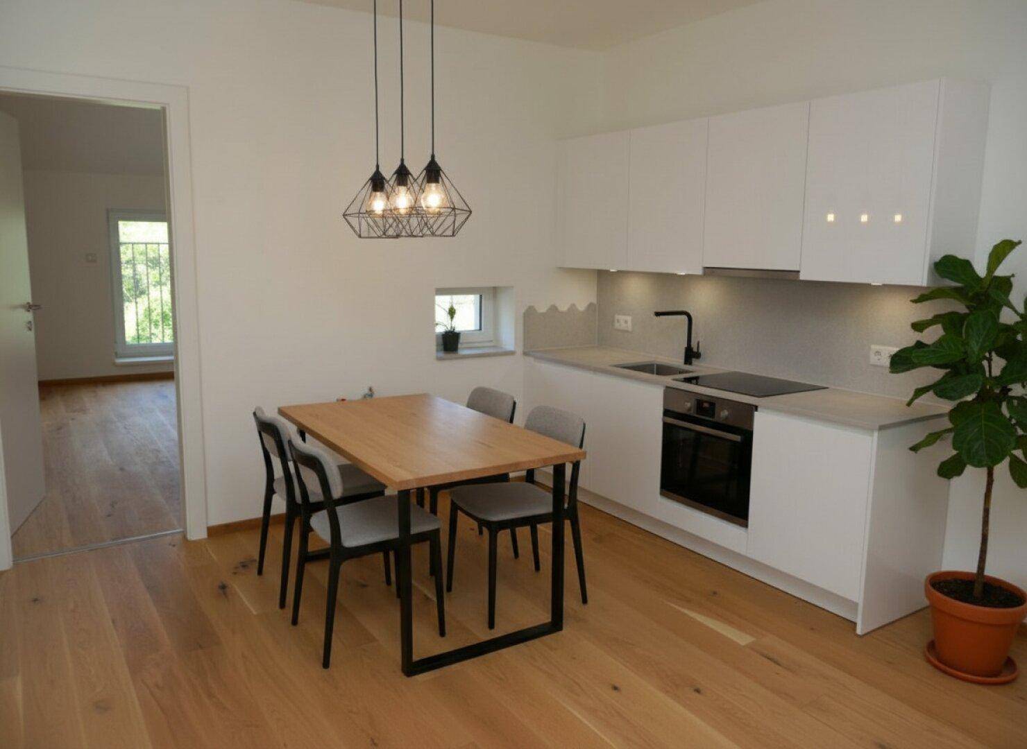 Moderne Küche mit weißen Schränken, Holztisch und Pendelleuchten, offen gestaltet.