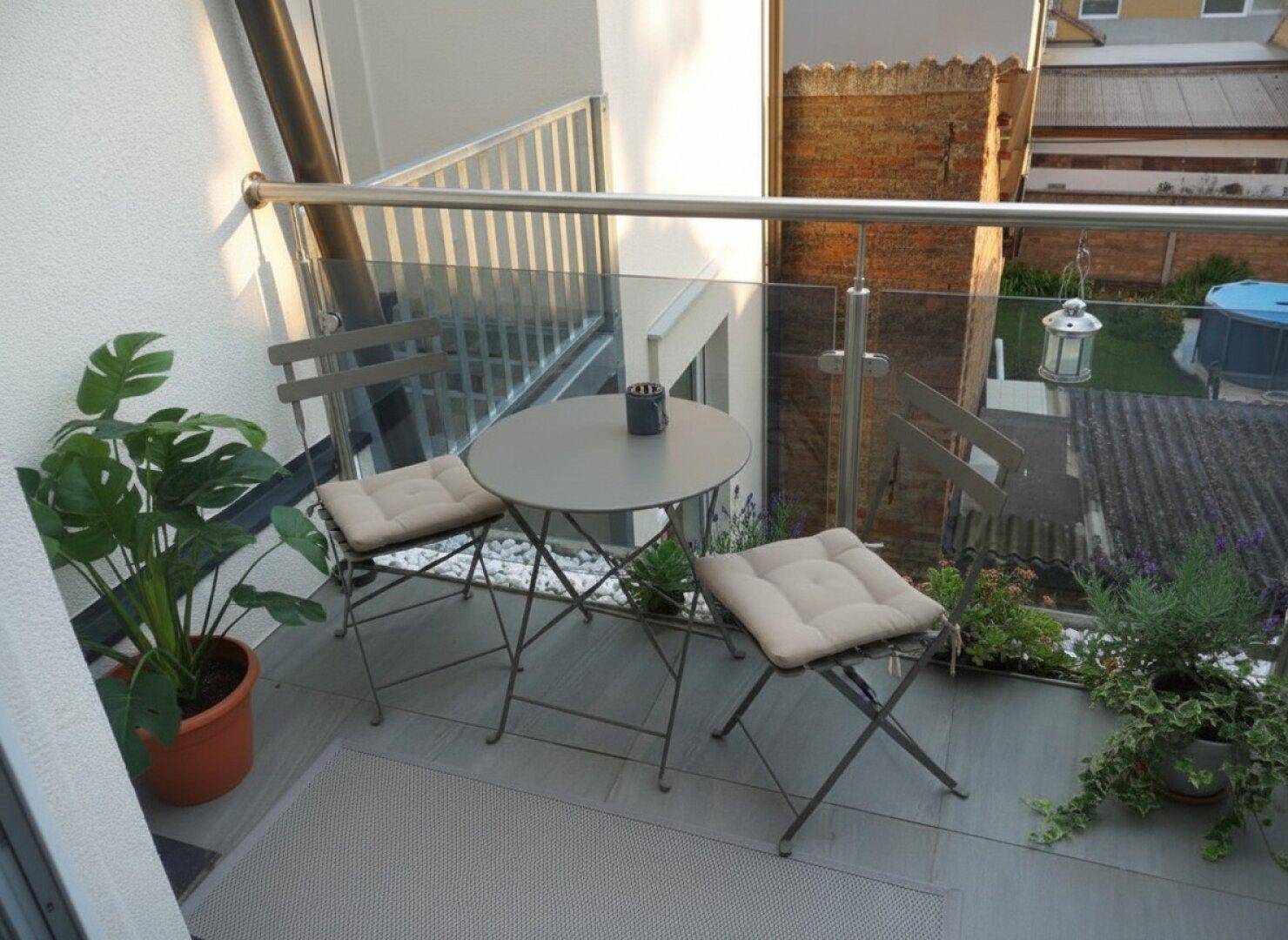 Kleiner Balkon mit Sitzgelegenheiten, Pflanzen und Blick auf die Nachbarschaft.