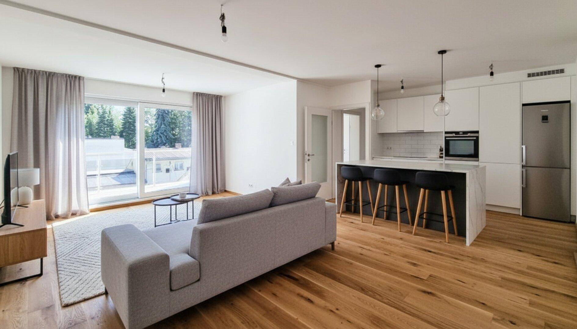 Heller offener Wohnbereich mit moderner Küche, Holzboden und Zugang zum Balkon.