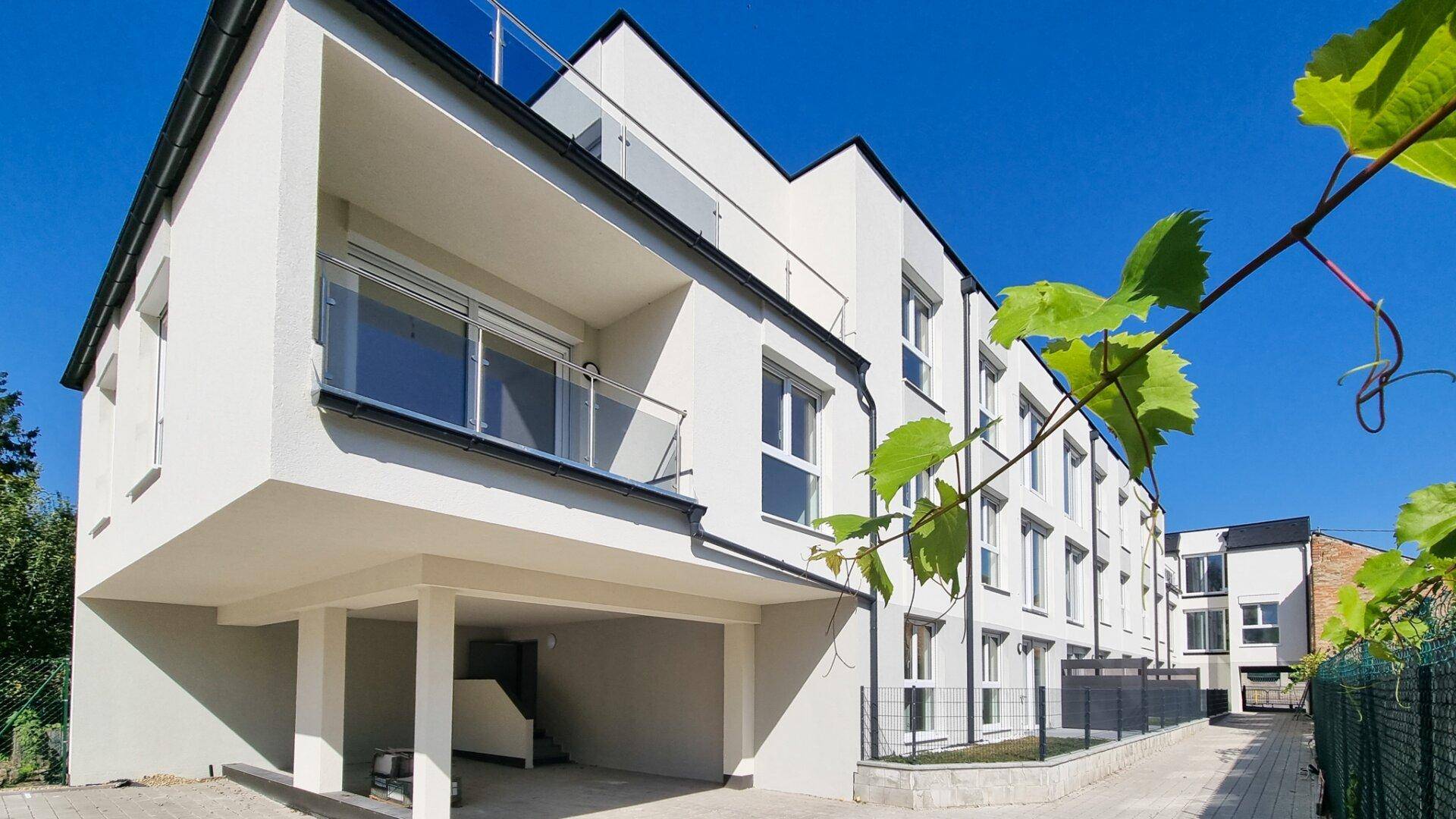 Seitenansicht eines modernen Wohngebäudes mit Balkonen und Carport unter strahlend blauem Himmel.