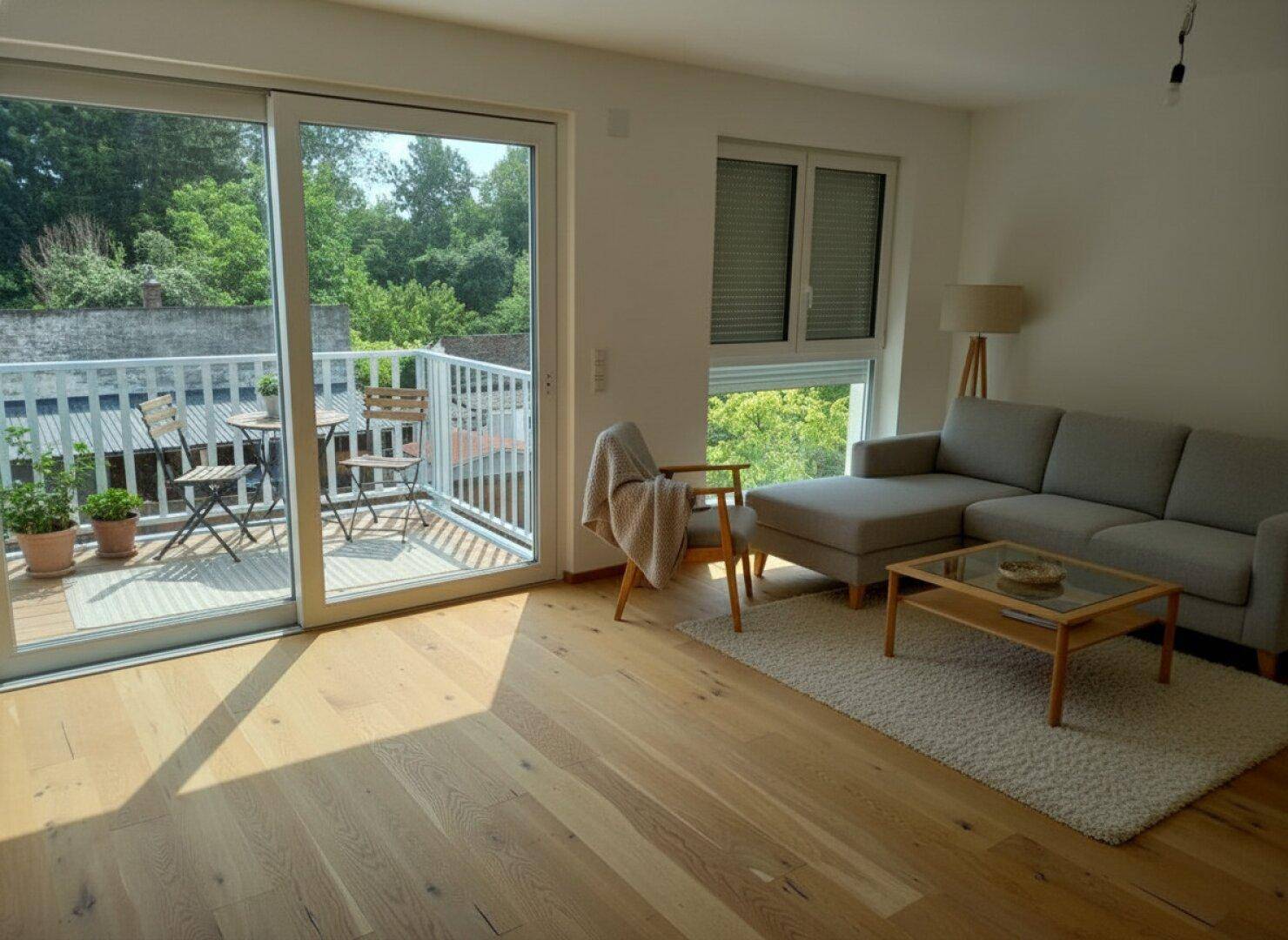 Helles Wohnzimmer mit Holzboden, bequemer Couch und Zugang zu einem möblierten Balkon.