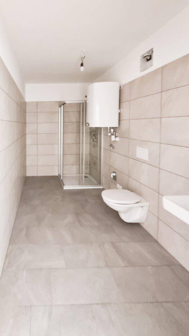 Modernes Badezimmer mit beigefarbenen Fliesen, Dusche und wandhängendem WC.