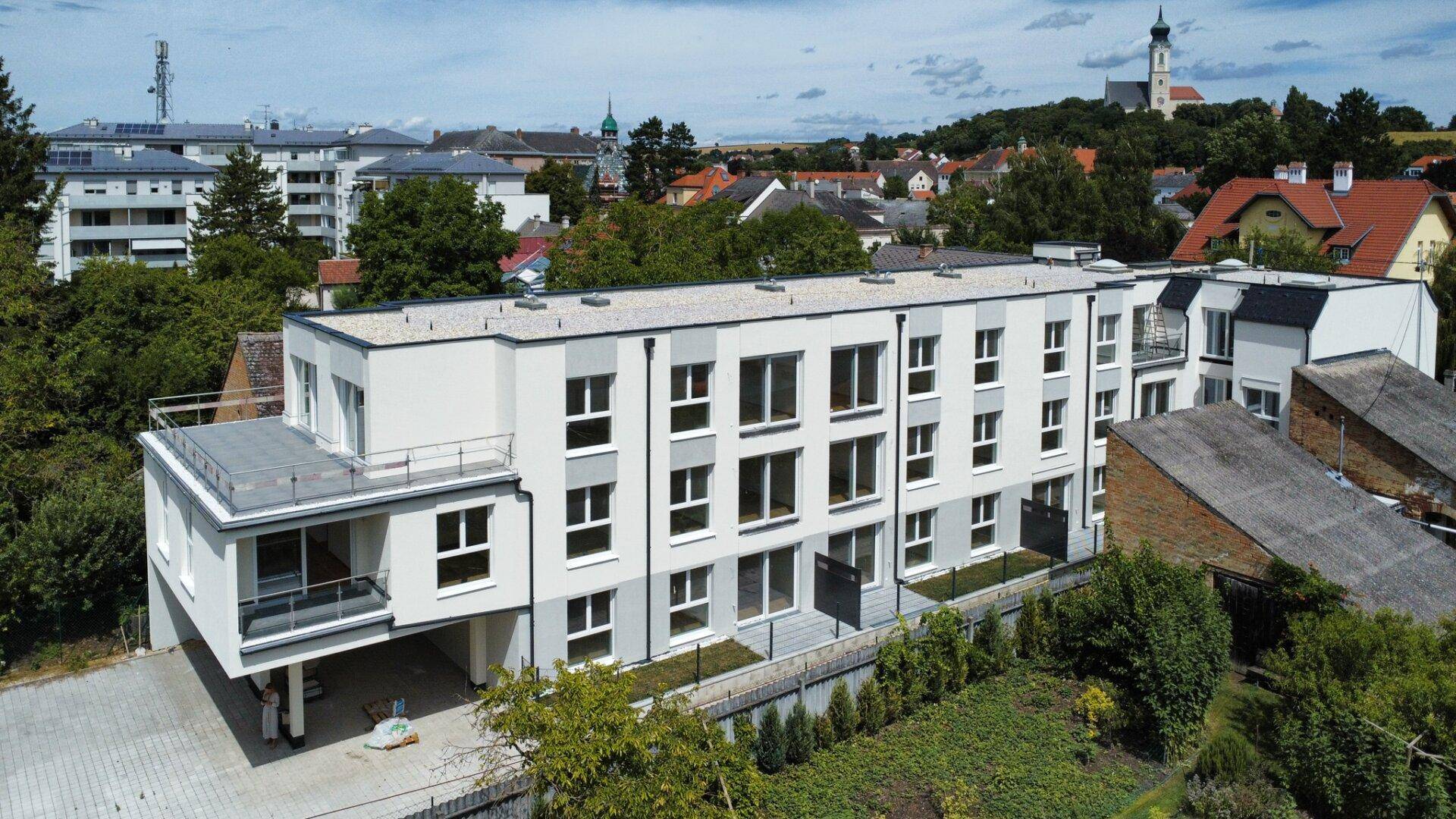 Luftaufnahme einer modernen Wohnanlage mit Flachdach und umliegender grüner Landschaft.