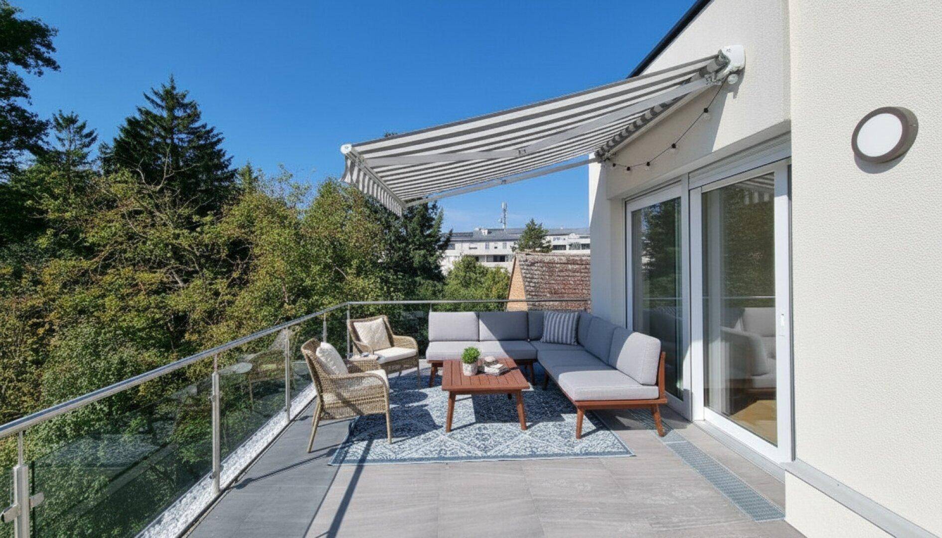 Gemütlicher Balkon mit Markise, Sitzgelegenheiten und Blick auf die grüne Umgebung.