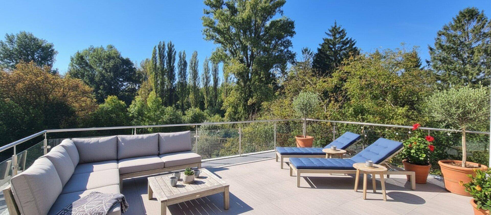 Sonnige Dachterrasse mit Liegestühlen, Loungemöbeln und weitem Blick ins Grüne.