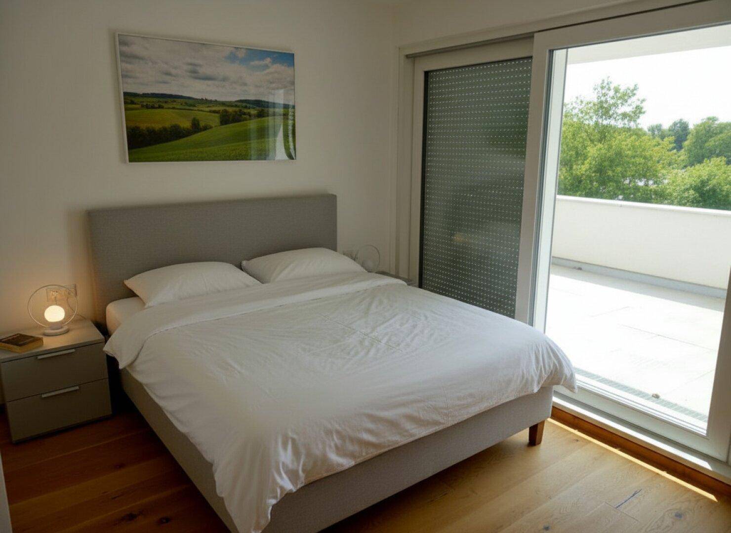 Helles Schlafzimmer mit Holzboden, Doppelbett und großem Schiebetürzugang zur Terrasse.