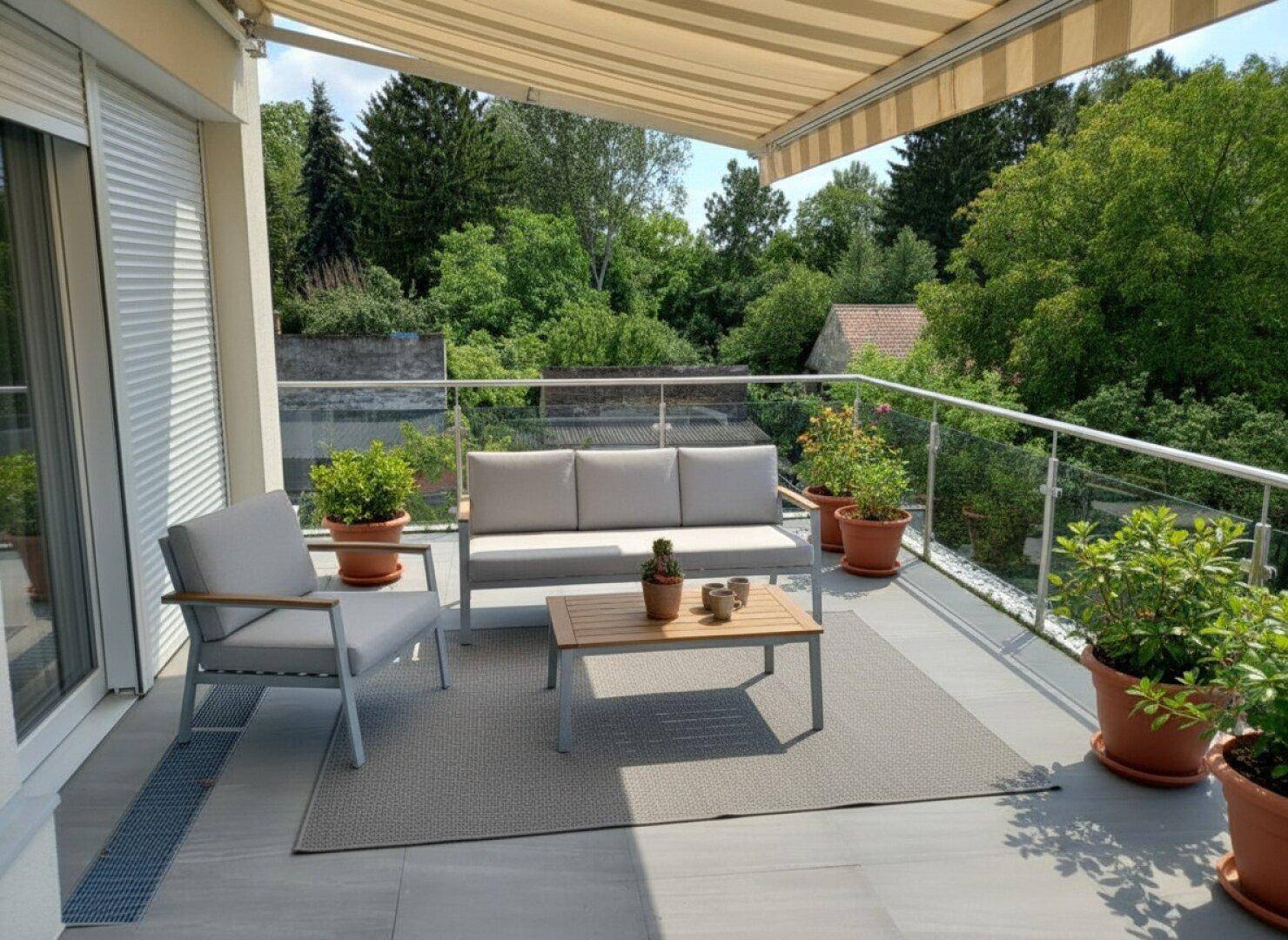 Heller Balkon mit Markise, modernen Gartenmöbeln und Blick auf die umliegende Natur.