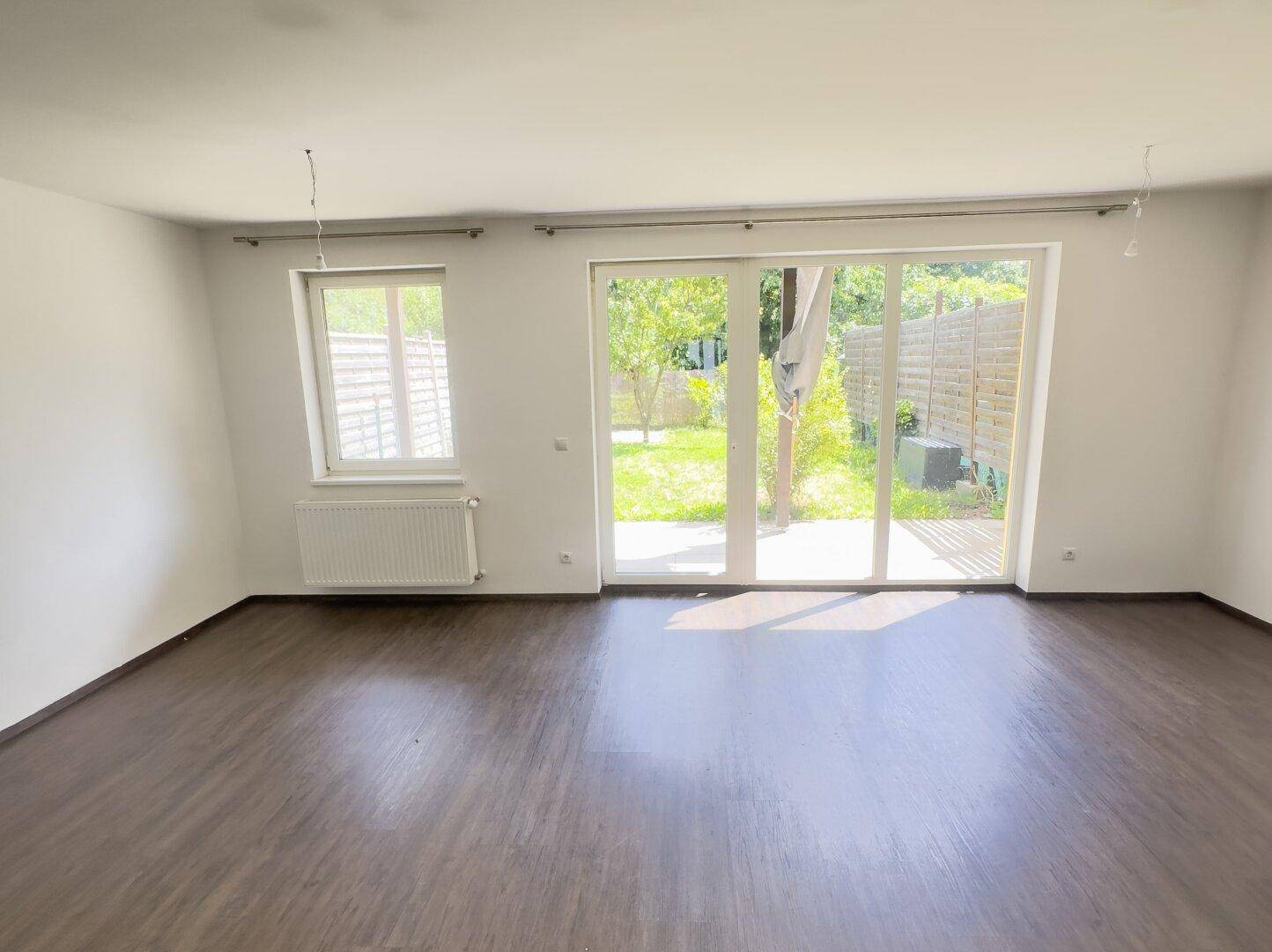 Heller Wohnraum mit Laminatboden und großem Zugang zum Garten durch eine Glastür.