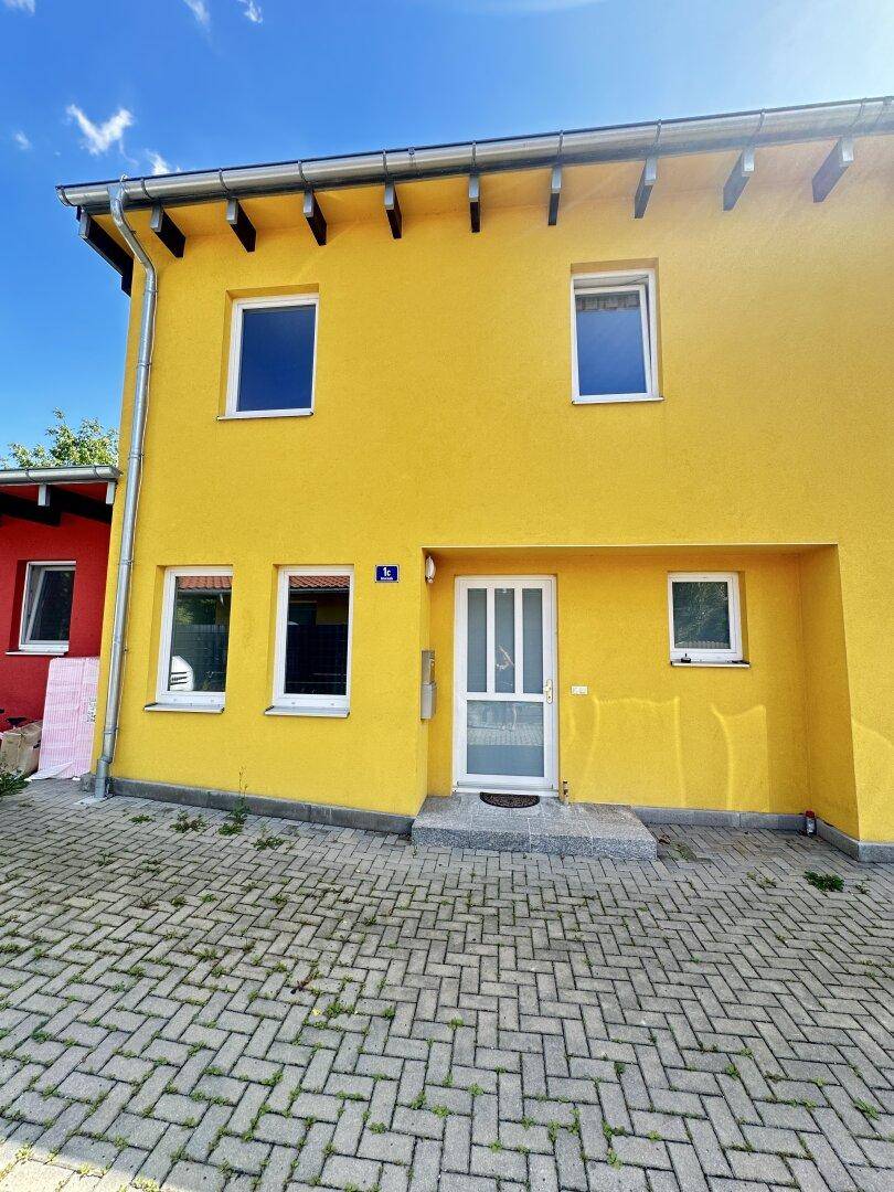 Vorderansicht eines gelben Einfamilienhauses mit gepflastertem Eingangsbereich und weißen Fenstern.