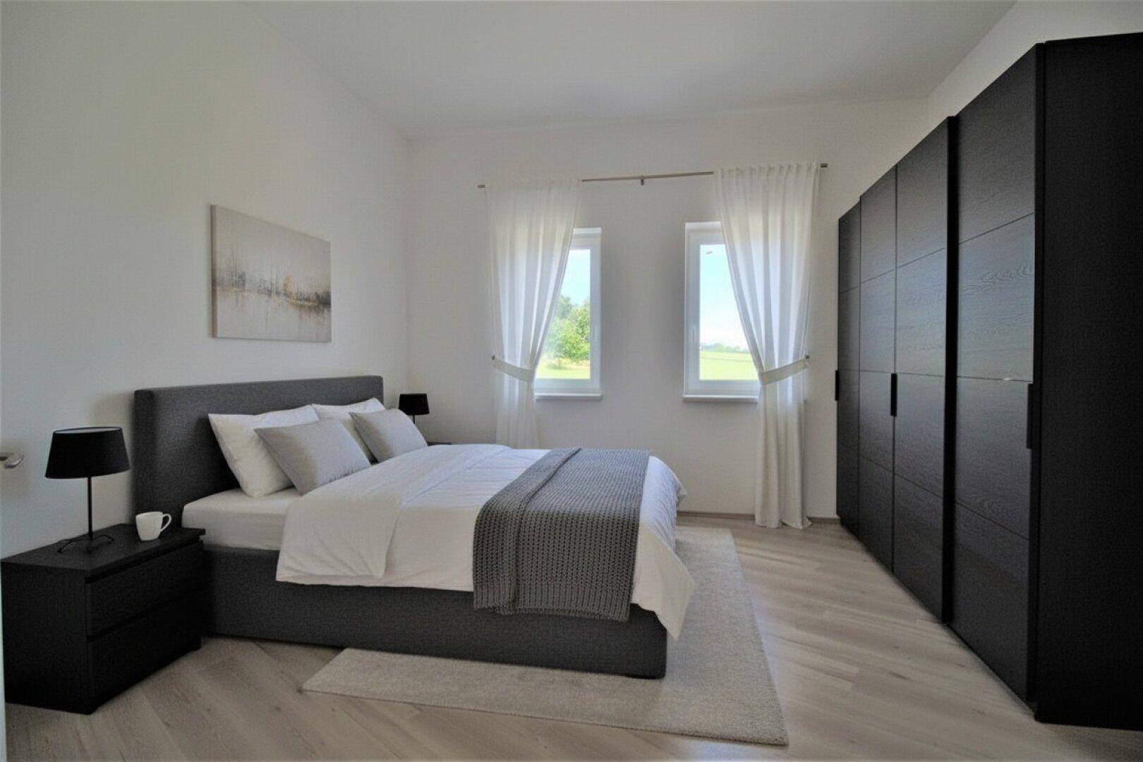 Schlafzimmer mit Doppelbett, dunklem Kleiderschrank und hellem Parkettboden.