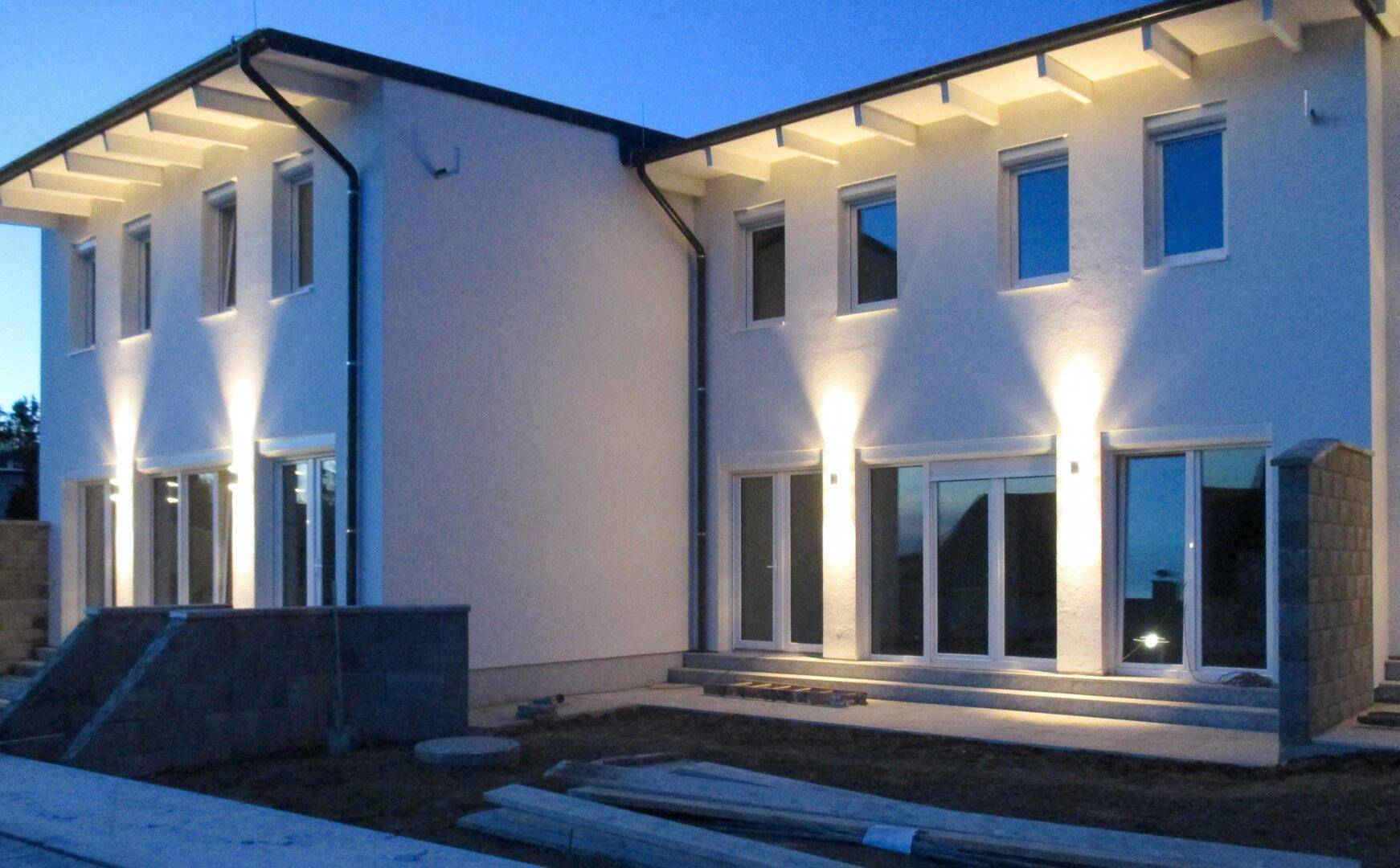 Beleuchtete Rückseite der Reihenhäuser bei Dämmerung mit Gartenbereichen.