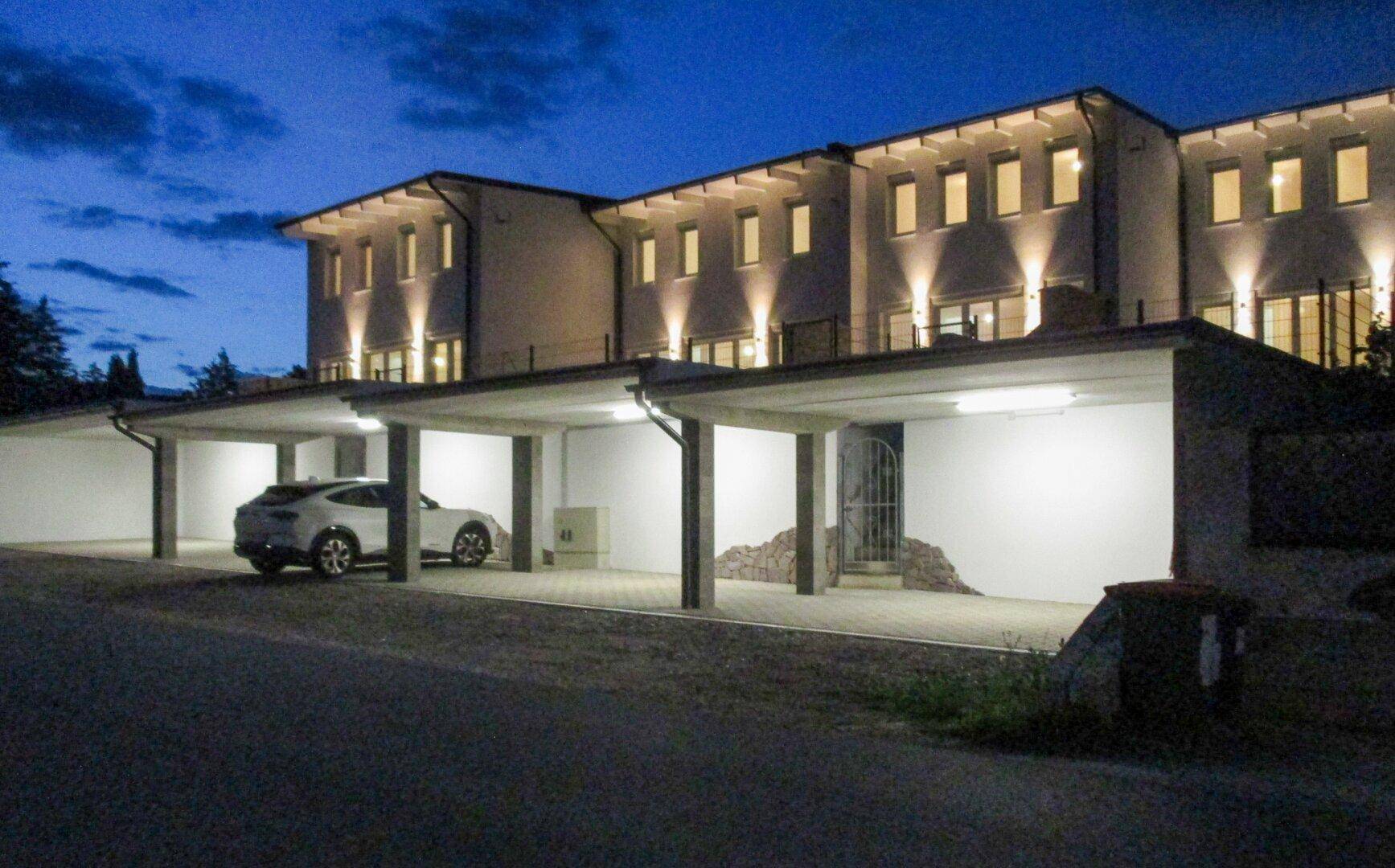 Beleuchtete Carports vor den Reihenhäusern in der Abenddämmerung.