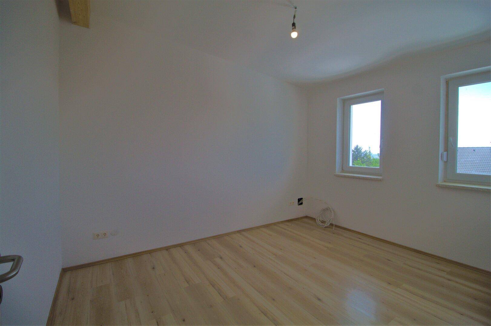 Leeres Schlafzimmer mit hellem Parkettboden und zwei Fenstern.