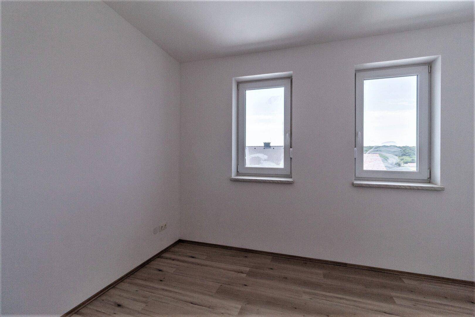 Unmöbliertes Zimmer mit hellem Parkettboden und Blick auf die Umgebung.