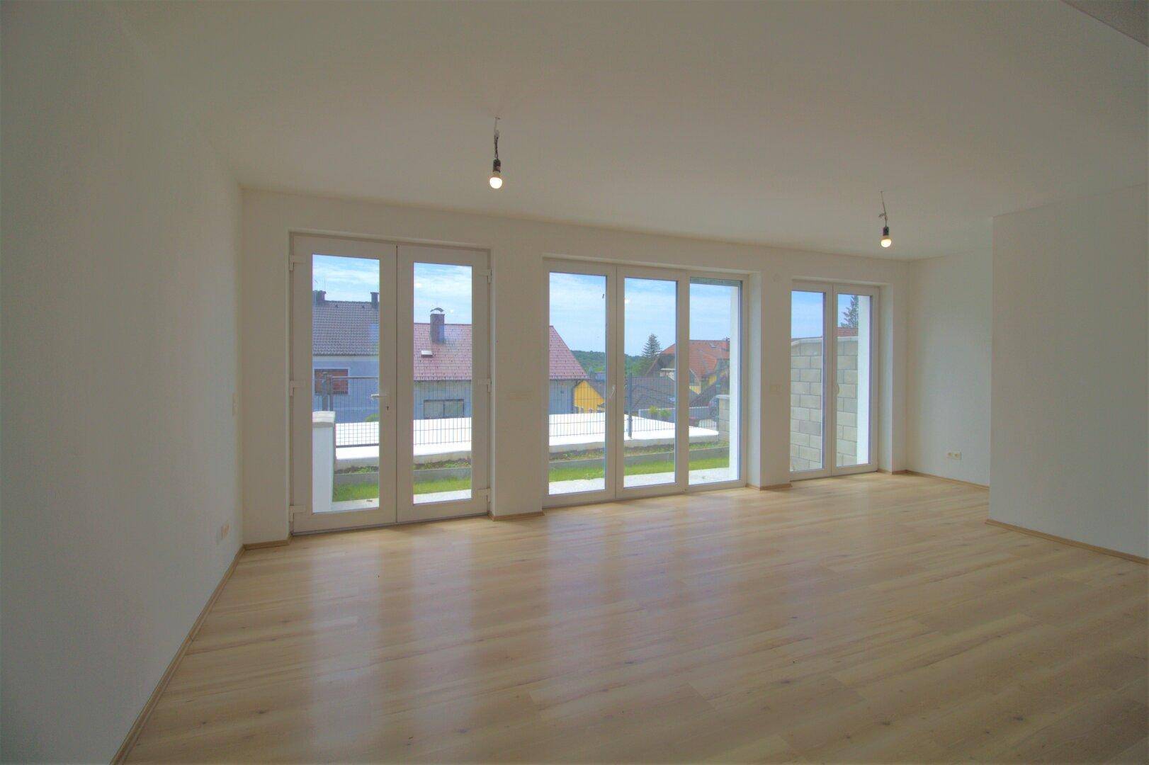 Geräumiges, leeres Wohnzimmer mit hellem Parkettboden und großen Fensterfronten.