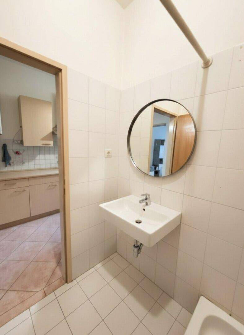 Modernes Badezimmer mit weißen Fliesen, einem einzelnen Waschbecken und rundem Spiegel.