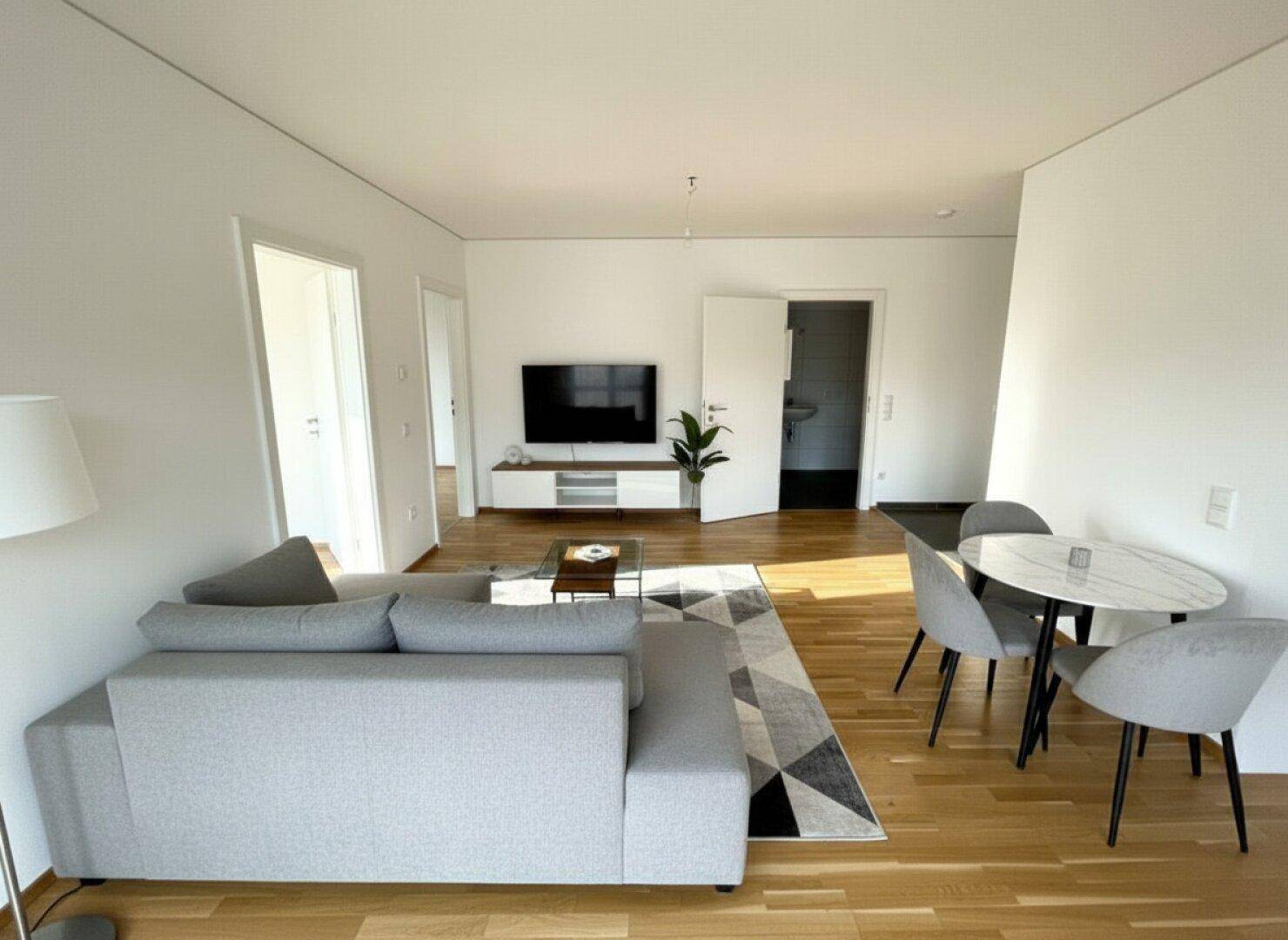 Heller Wohn- und Essbereich mit Parkettboden, modernem Sofa und Esstisch.