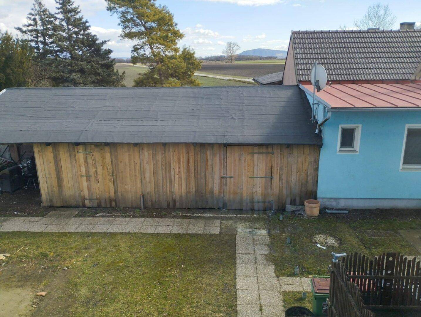 Langes Holzgebäude mit Flachdach neben dem blauen Haus, umgeben von Rasenfläche.