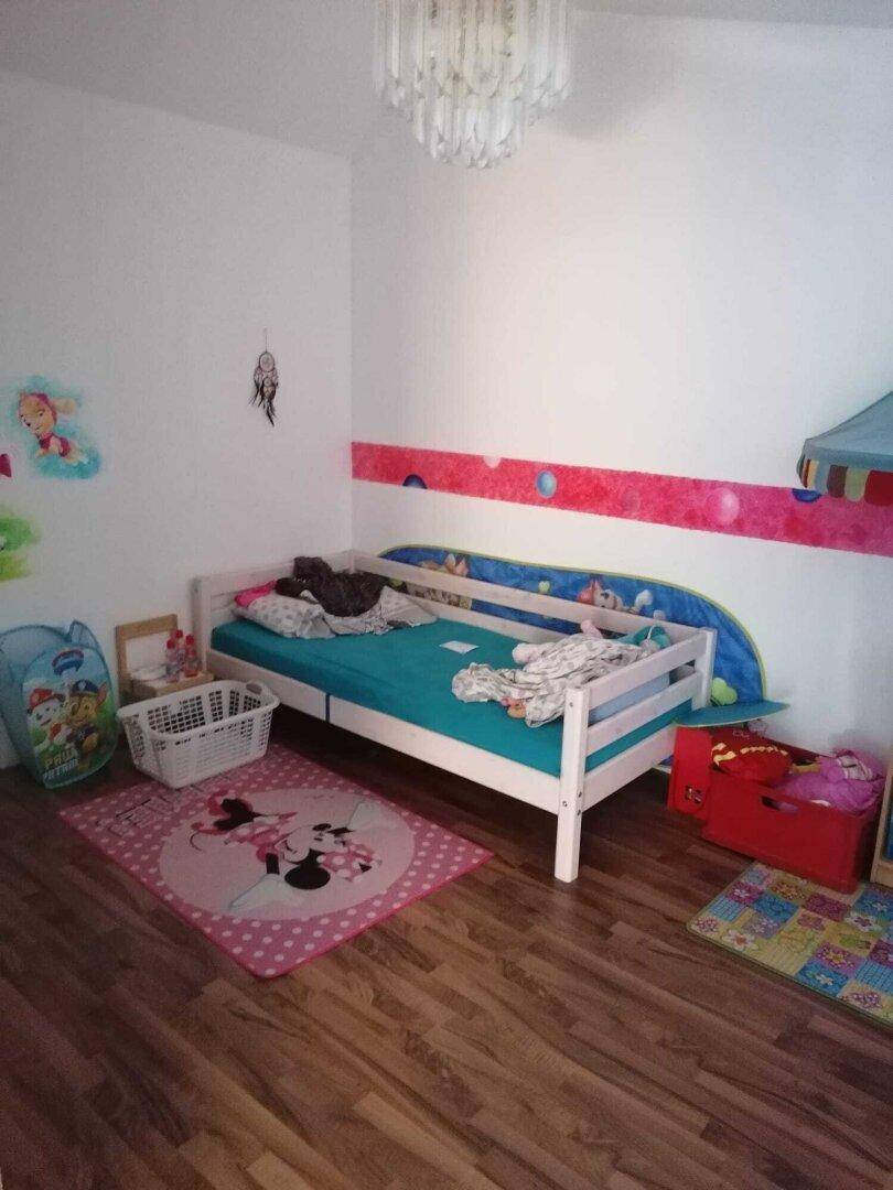 Kinderzimmer mit Einzelbett, Spielteppichen und farbenfroher Wanddekoration.