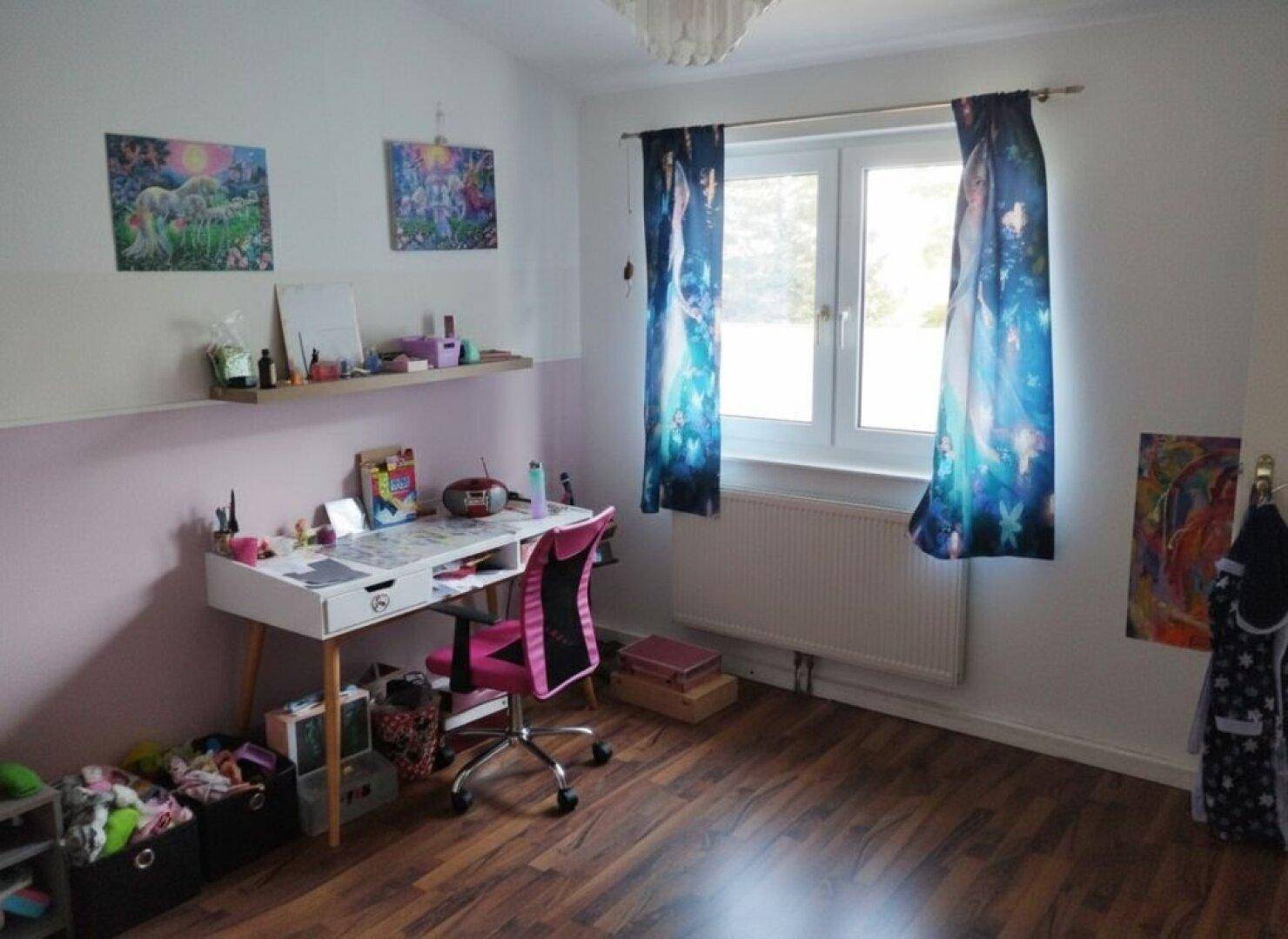 Kinderzimmer mit Schreibtisch, Fenster und Laminatboden, hell und funktional eingerichtet.