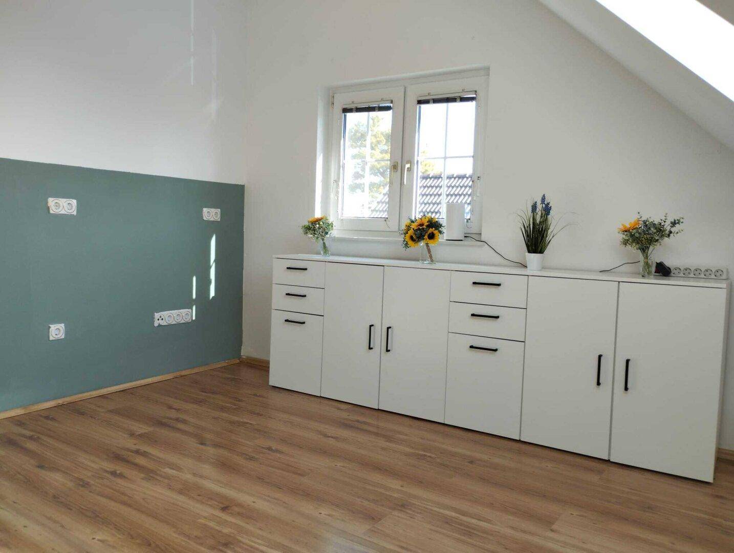 Dachgeschossraum mit Laminatboden, weißen Schränken und schräger Decke.