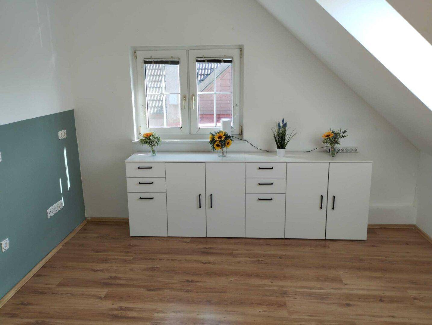 Heller Dachgeschossraum mit Einbauschränken unter dem Fenster und Laminatboden.