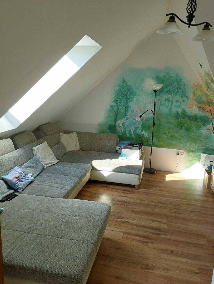 Helles Dachgeschoss-Wohnzimmer mit Sofa, Dachfenster und kreativer Wandmalerei.