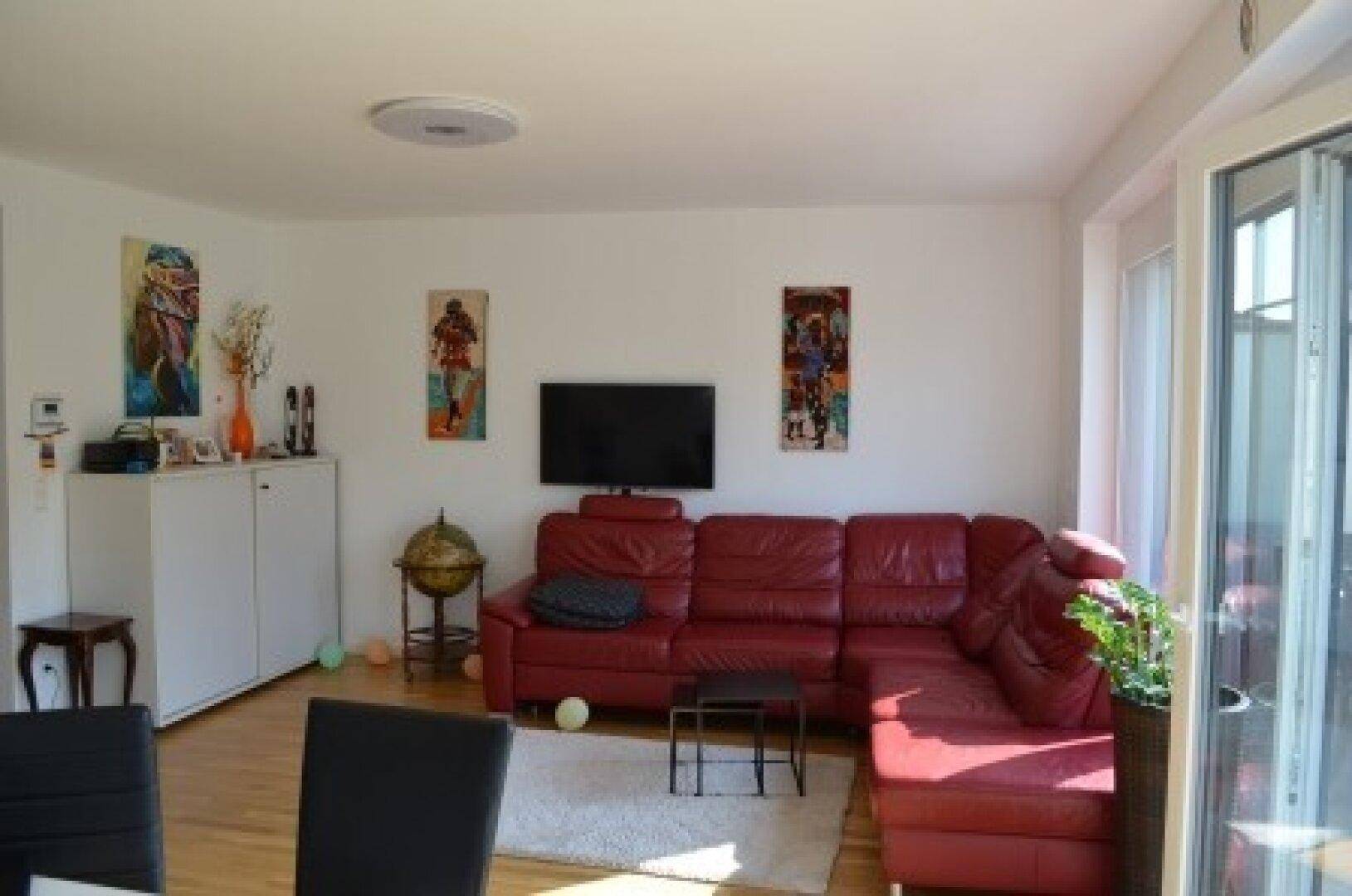 Heller Wohnbereich mit rotem Ledersofa, Holzboden und Zugang zum Essbereich, geschmückt mit moderner Kunst.