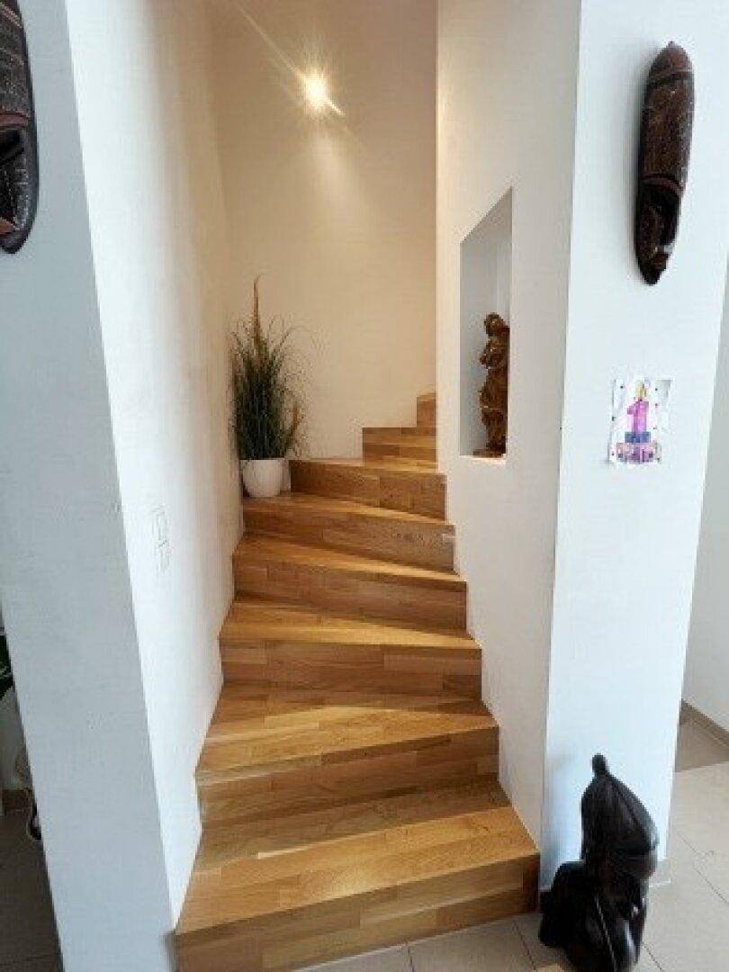 Elegante Holztreppe mit hellen Wänden und indirekter Beleuchtung, die die oberen Etagen verbindet.