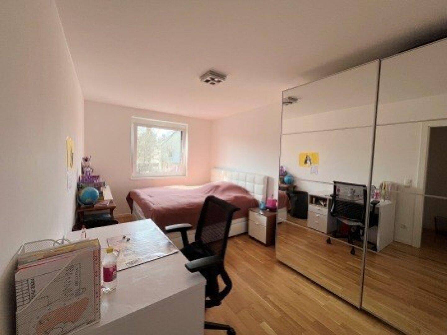 Geräumiges Schlafzimmer mit Holzboden, Bett, Schreibtisch und einem großen Spiegelschrank für viel Stauraum.