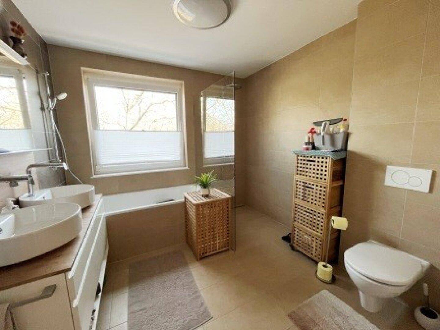 Modernes Badezimmer mit beigen Fliesen, Doppelwaschbecken, Badewanne, Dusche und großem Fenster.