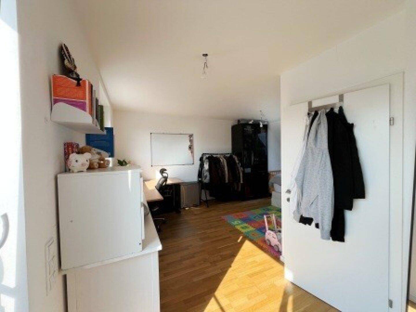 Vielseitiger Raum im Dachgeschoss mit Holzboden, Schreibtisch und Stauraum, ideal als Büro oder Spielzimmer.