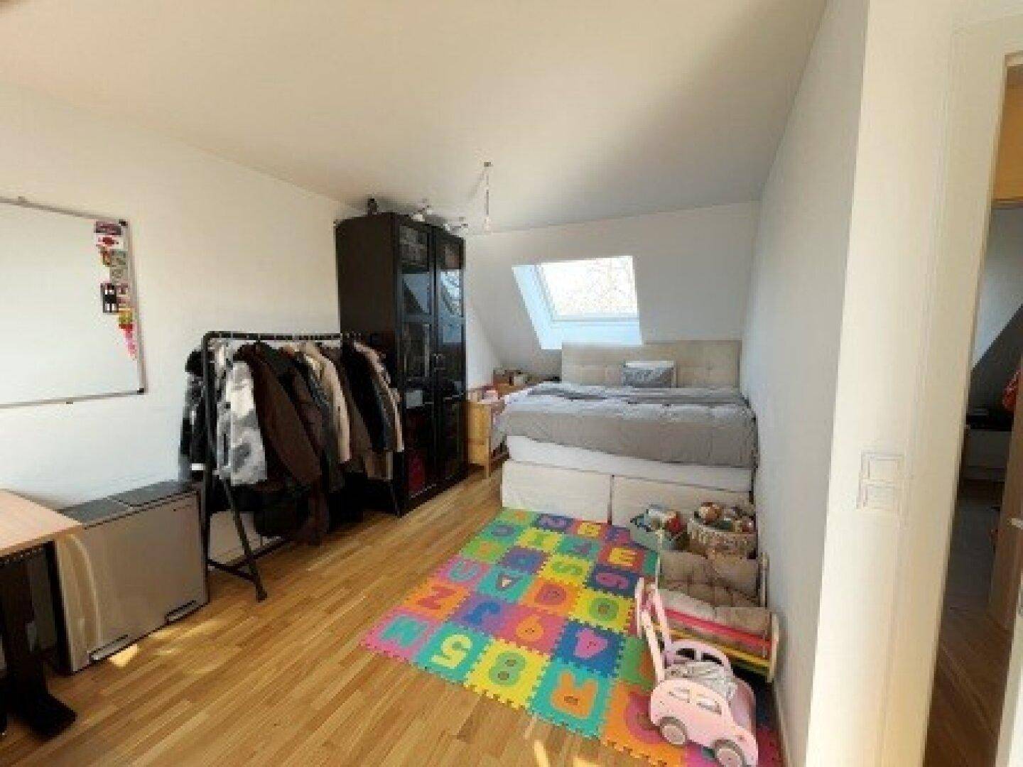 Gemütlicher Dachgeschossraum mit Bett, Holzboden und Dachfenster, das viel natürliches Licht hereinlässt.