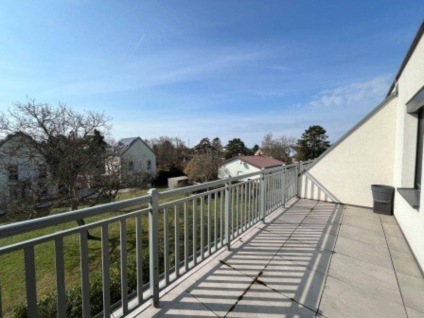 Geräumiger Balkon mit Fliesenboden und weitem Blick über die umliegende Wohngegend unter blauem Himmel.
