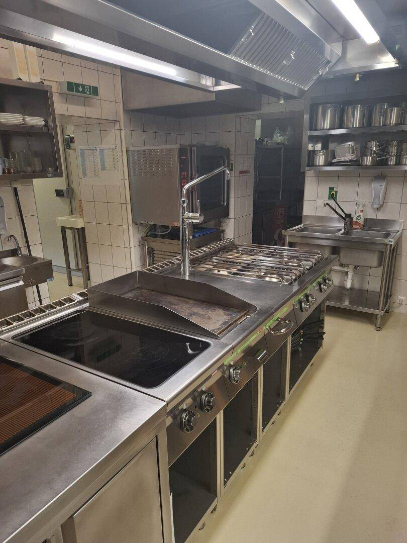 Professionelle Großküche mit Edelstahlgeräten, Induktionskochfeld und Dunstabzugshaube für den Gastronomiebetrieb.