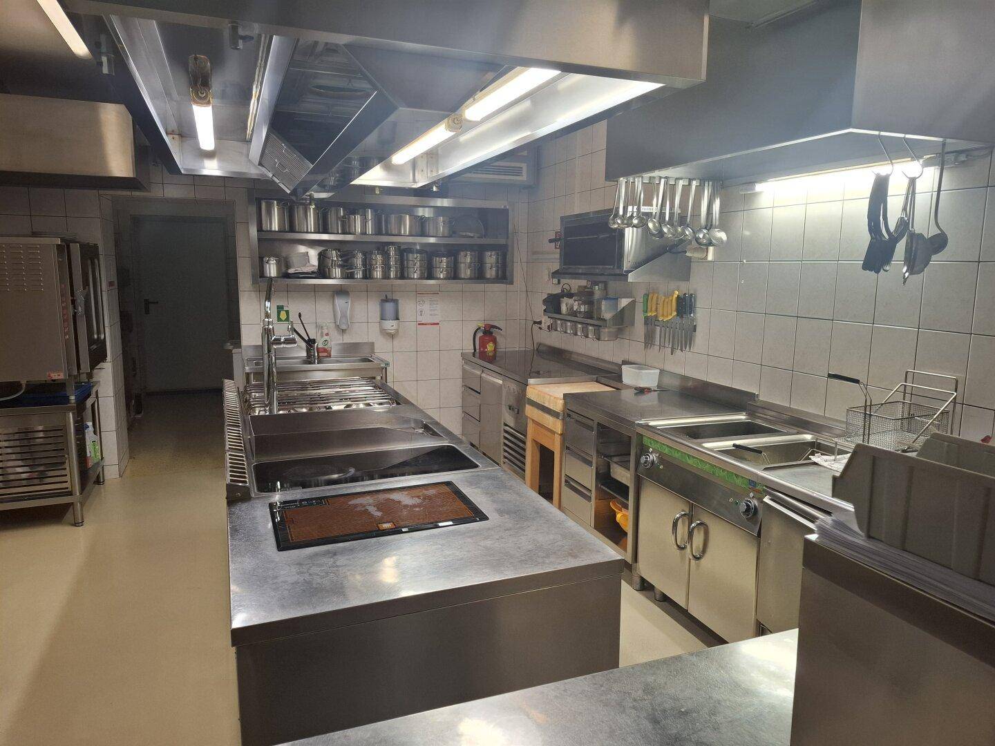 Geräumige Industrieküche mit umfangreicher Ausstattung, vielen Arbeitsflächen und professionellen Kochgeräten.