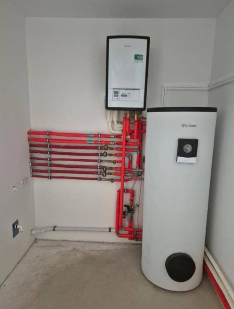Technikraum mit Warmwasserspeicher und sichtbaren roten Rohren für die Fußbodenheizung.