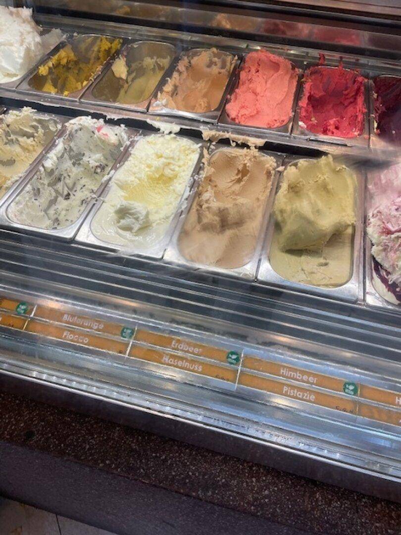 Nahaufnahme einer Eistheke mit verschiedenen Eissorten und Beschriftungen der Geschmacksrichtungen.