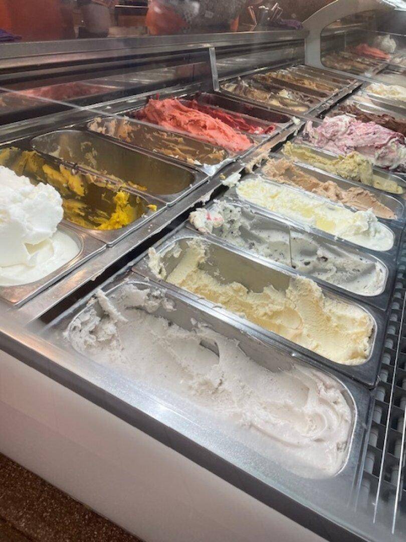 Weitere Nahaufnahme einer Eistheke mit vielen verschiedenen Eissorten, einige davon bereits angebrochen.