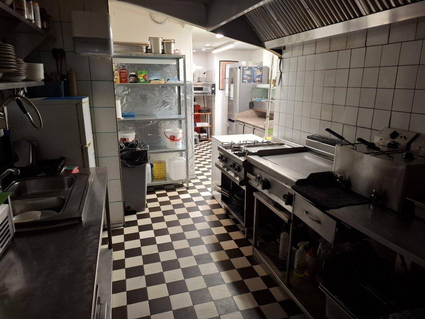 Professionelle Großküche mit Edelstahlgeräten, kariertem Fliesenboden und gefliesten Wänden.