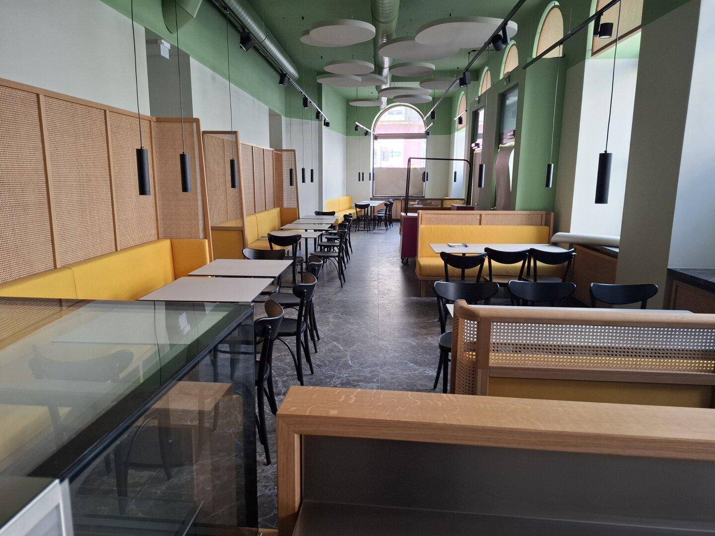 Geräumiger Restaurantbereich mit modernen gelben Sitzbänken, Holzakzenten und einer langen Theke mit Glasvitrine.