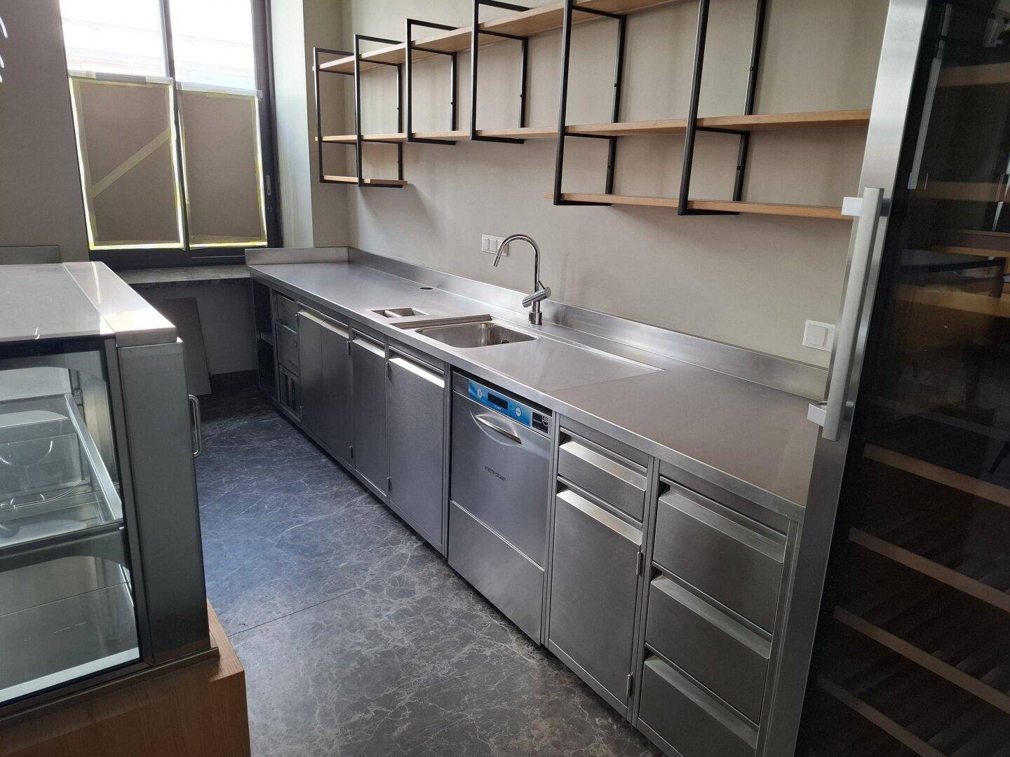 Moderner Edelstahl-Küchenbereich mit integriertem Geschirrspüler, Spülbecken und offenen Holzregalen über dunklem Boden.