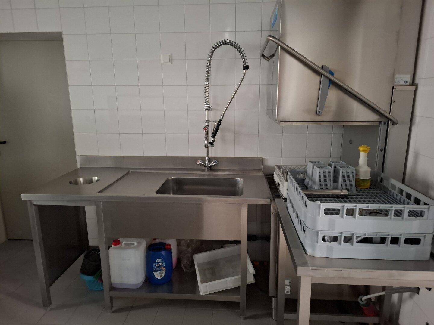 Spülbereich einer Großküche mit großem Edelstahlbecken, professioneller Armatur und weißen Fliesenwänden.