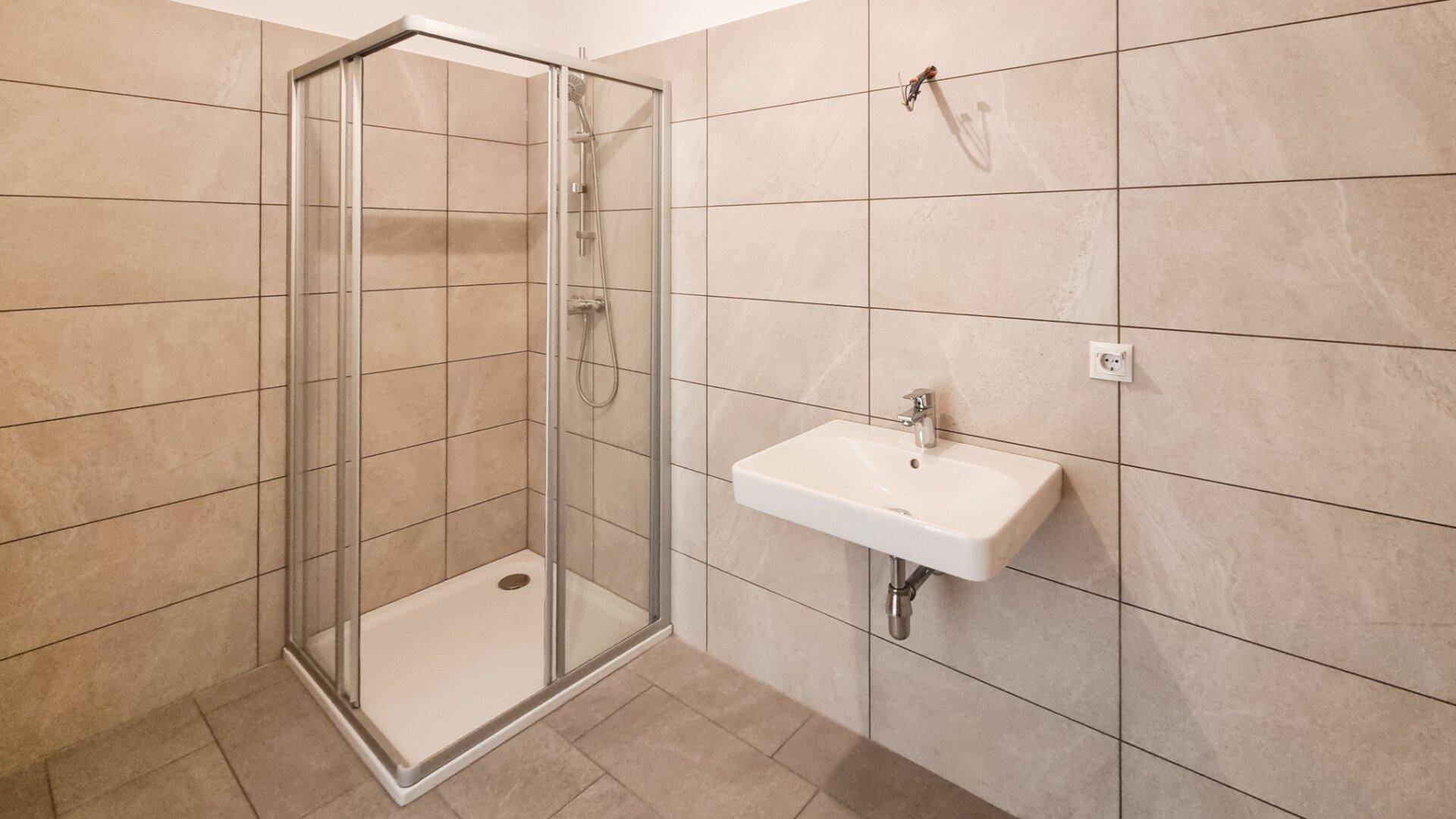Modernes Badezimmer mit Duschkabine und wandhängendem Waschbecken, hell gefliest.