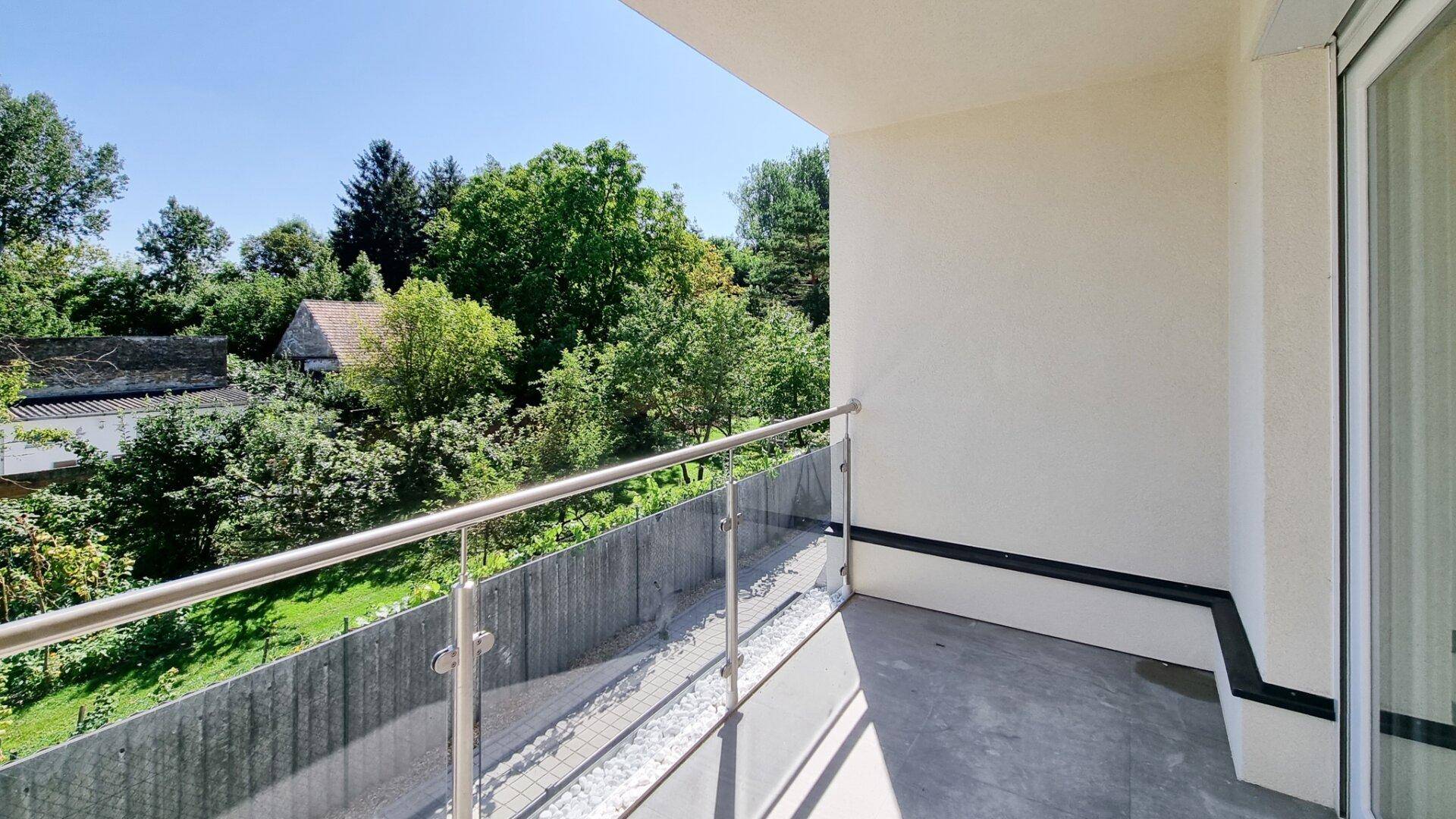 Heller Balkon mit Glasgeländer und Blick ins Grüne, ideal zum Entspannen im Freien.