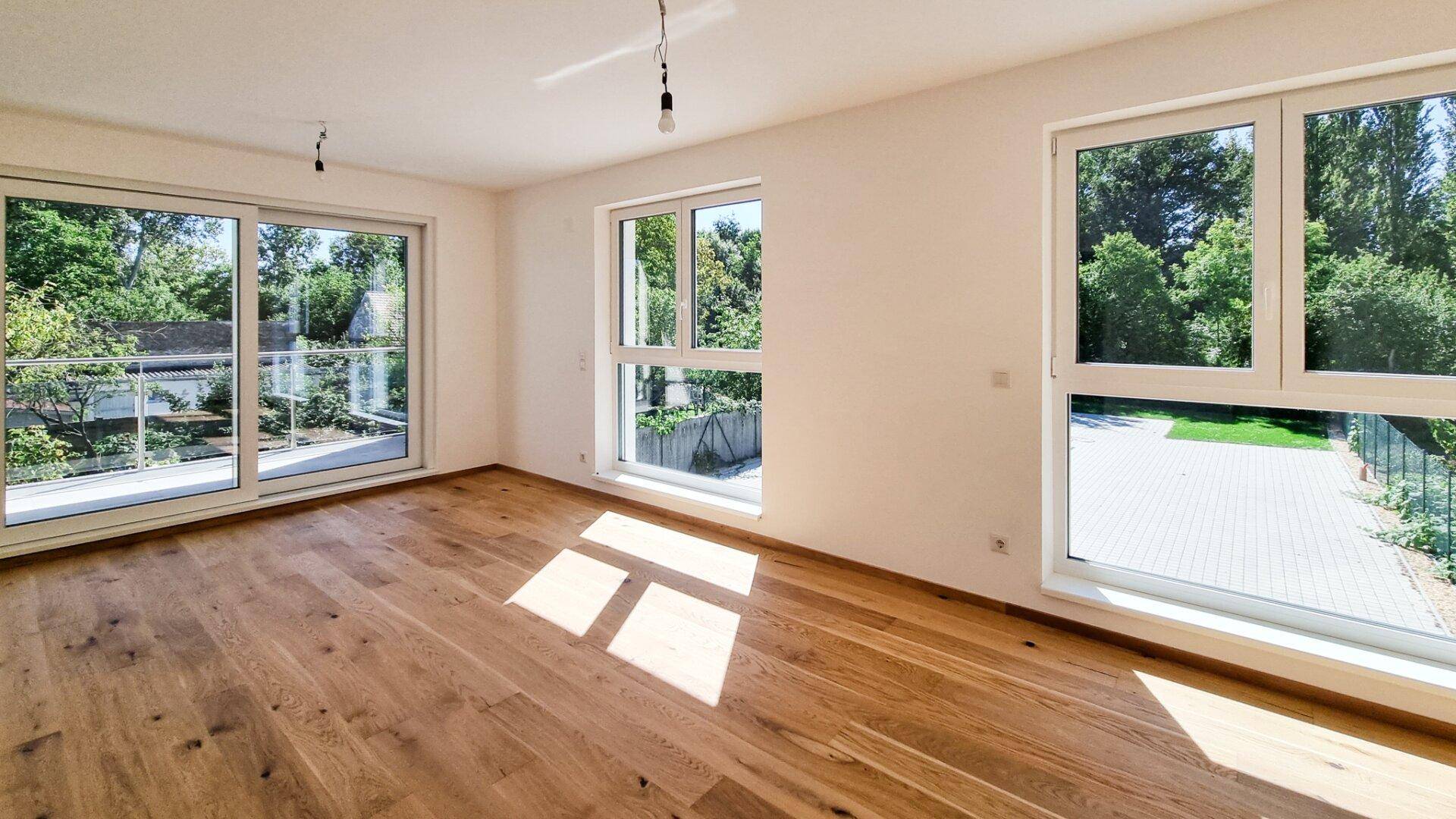 Heller, leerer Raum mit Holzboden und großen Schiebetüren zum Balkon, viel Tageslicht.