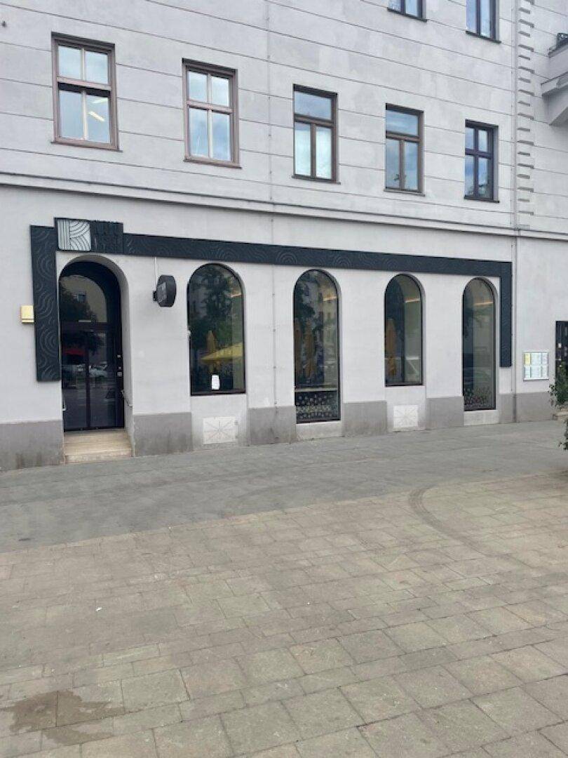 Nahaufnahme einer Gebäudefassade mit großen Bogenfenstern und einem Haupteingangsbereich.